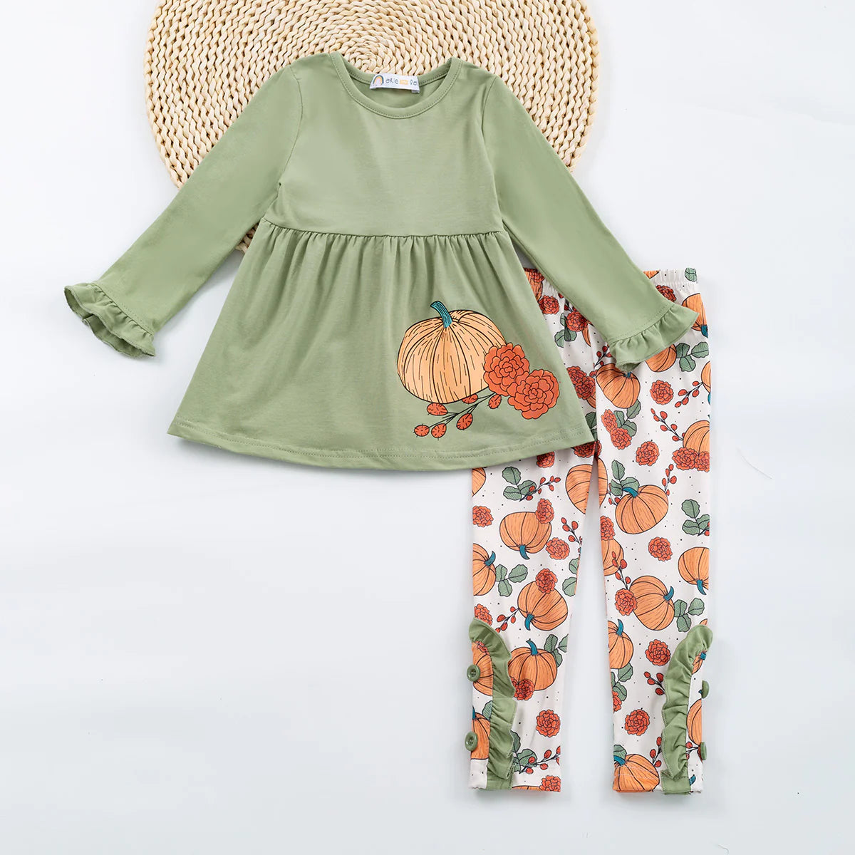 A green outfit with orange and black accents, featuring a round neckline and three-quarter sleeves, displayed with matching pumpkin-patterned pants.